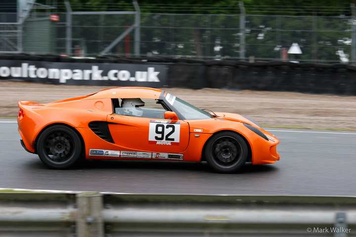 An orange Lotus Elise racing at Oulton Park