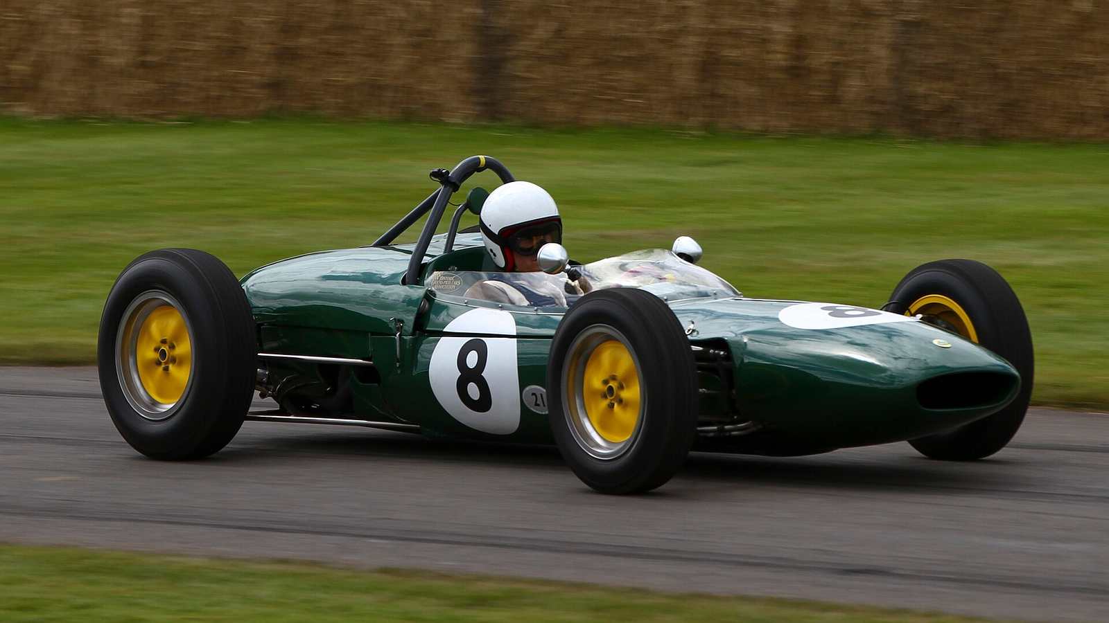 A green Lotus 21 Formula 1 car with yellow wheels and the number 8, driven past straw bales at the Goodwood Festival of Speed