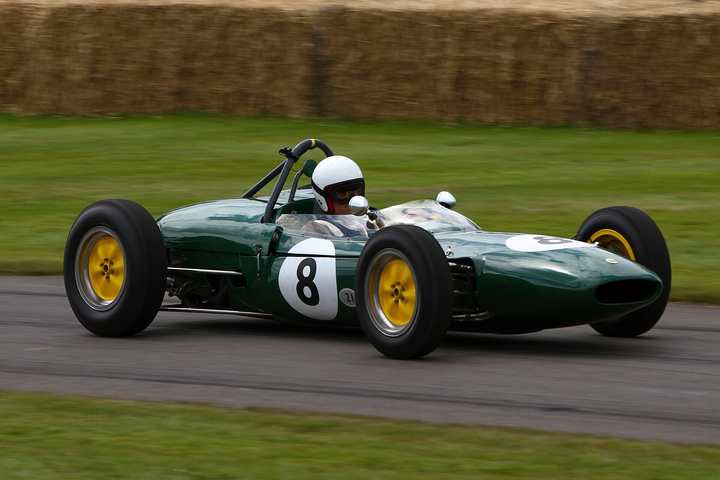 A green Lotus 21 Formula 1 car with yellow wheels and the number 8, driven past straw bales at the Goodwood Festival of Speed